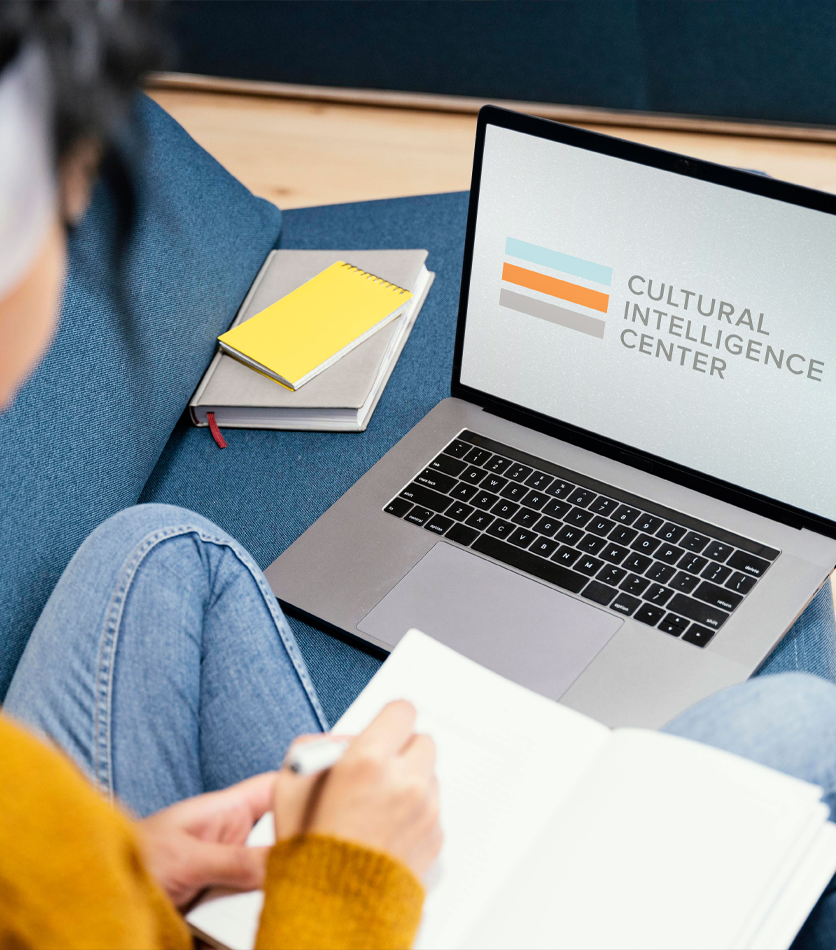 Person studying on a couch with a laptop showing the Cultural Intelligence Center logo and a notebook beside it.