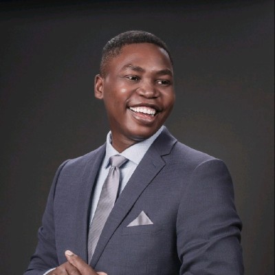 Man in a navy suit smiling warmly, looking slightly to the side, against a dark gradient background.