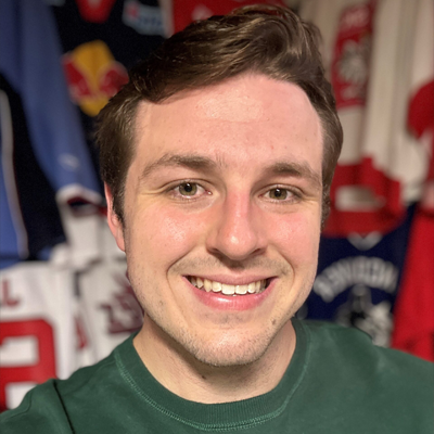 Smiling man in a green shirt taking a close-up portrait, colorful sports jerseys in the background.