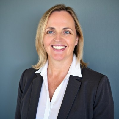 Smiling woman in a black blazer and white blouse against a blue backdrop.