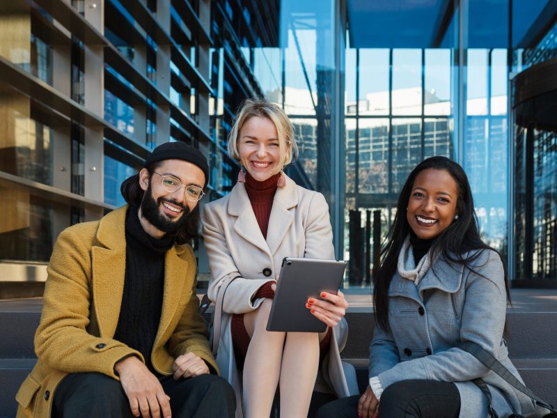 business-colleagues-looking-at-camera-and-smile-while-sitting-on-the-stairs-outside-the-office.jpg